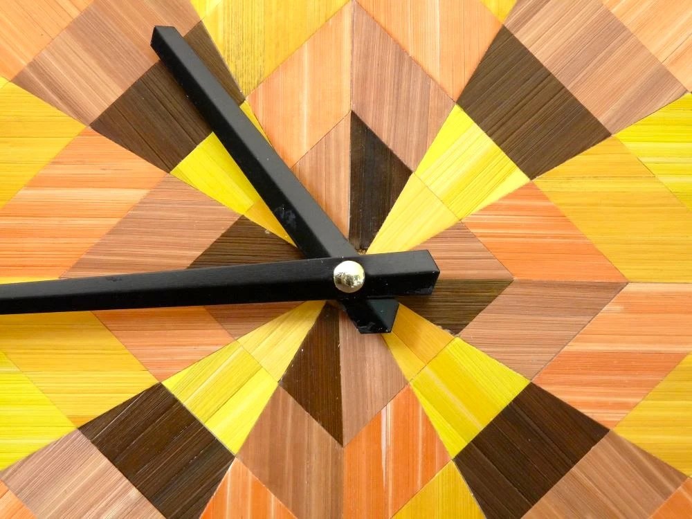 Centre de l'horloge géométrique décorée en marqueterie de paille. couleurs chaudes : jaune citron, jaune or, marron, orange et cuivre.