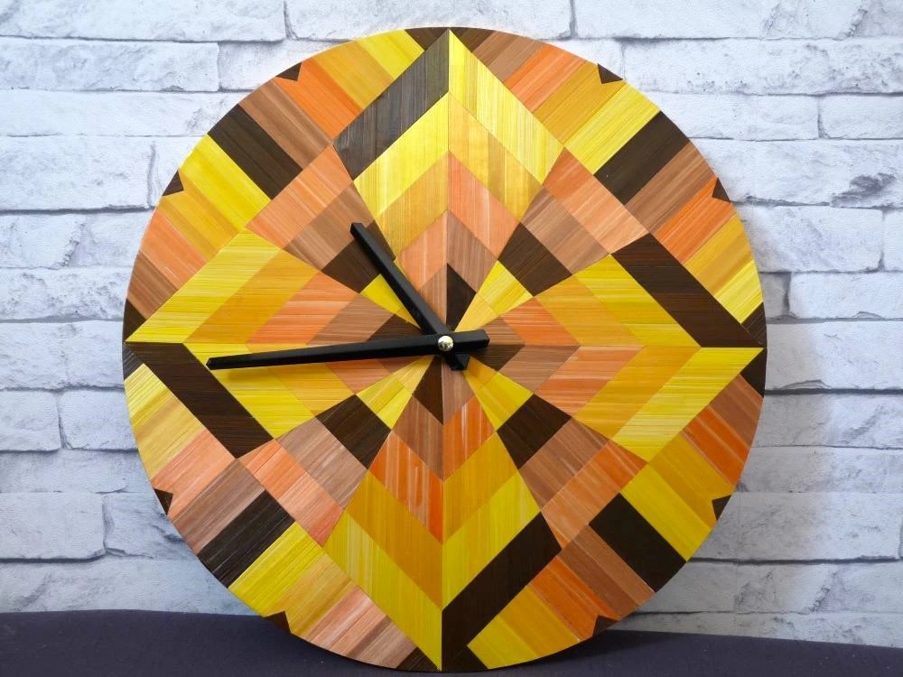 Horloge géométrique décorée en marqueterie de paille. couleurs chaudes : jaune citron, jaune or, marron, orange et cuivre
