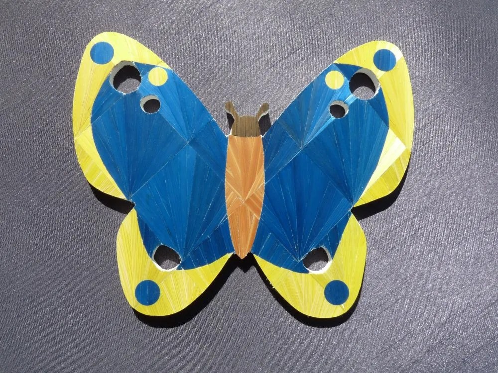 Papillon en marqueterie de paille de couleur bleue et jaune sur les bords.